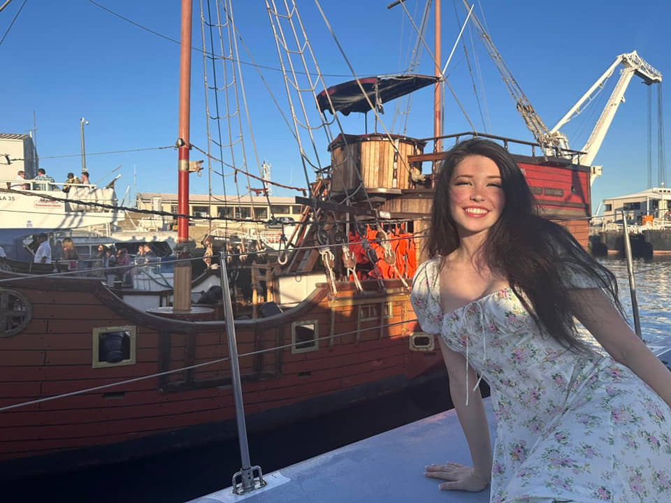 Portside photo of Belle Delphine in a floral dress, smiling for the camera.