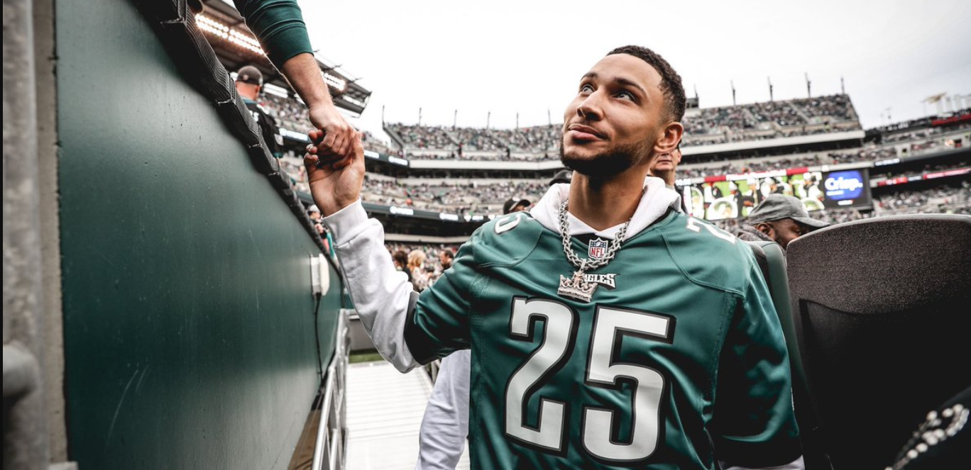 Ben Simmons in a jersey holding a fan's hand and smiling.