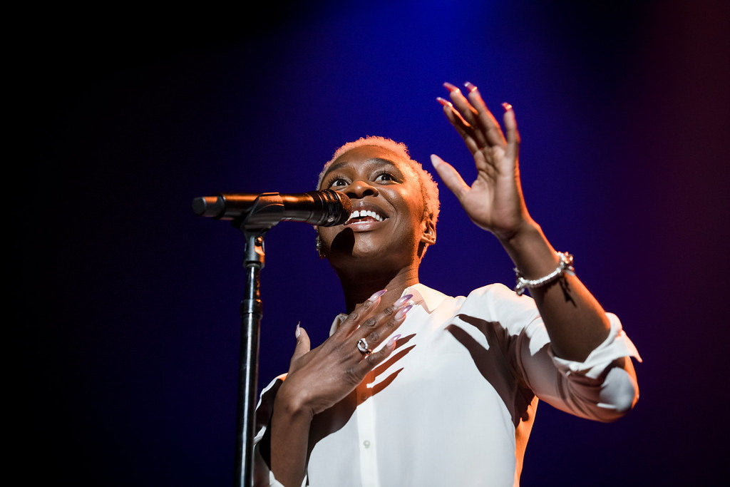 Cynthia Erivo wearing a white shirt and singing at her concert.