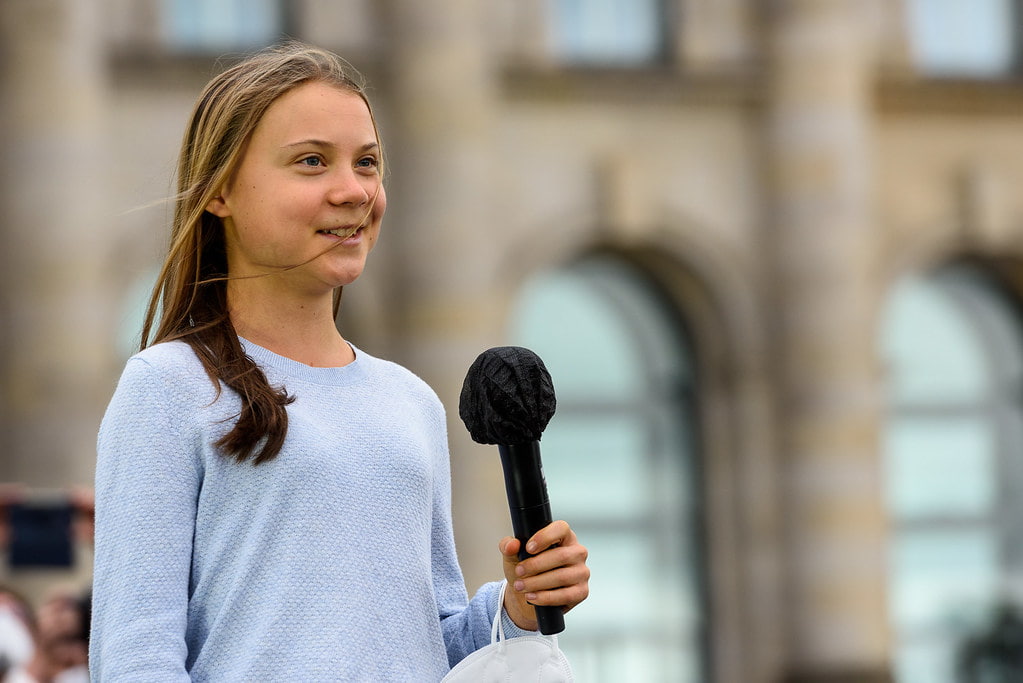 Greta Thunberg in a blue top, holding a mic while speaking.