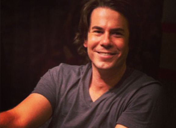 Jerry Trainor with long brown hair smiling at the camera.