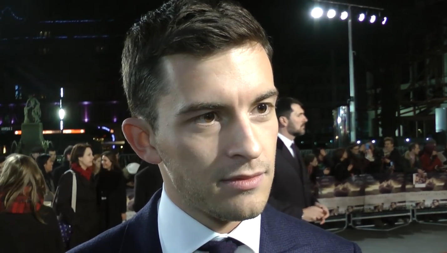 Jonathan Bailey in a suit at a nighttime event, surrounded by a crowd and bright lights.