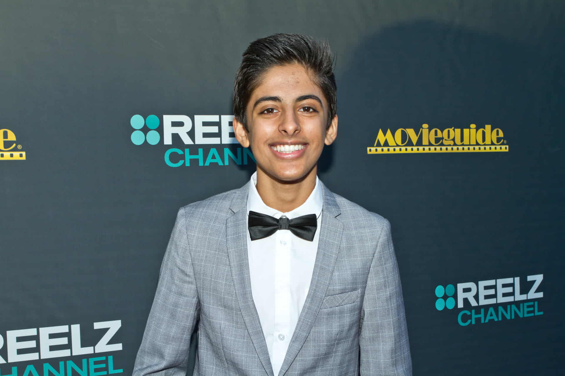 Karan Brar, smiling for the camera, waring a grey suit and a black bow tie at an event.
