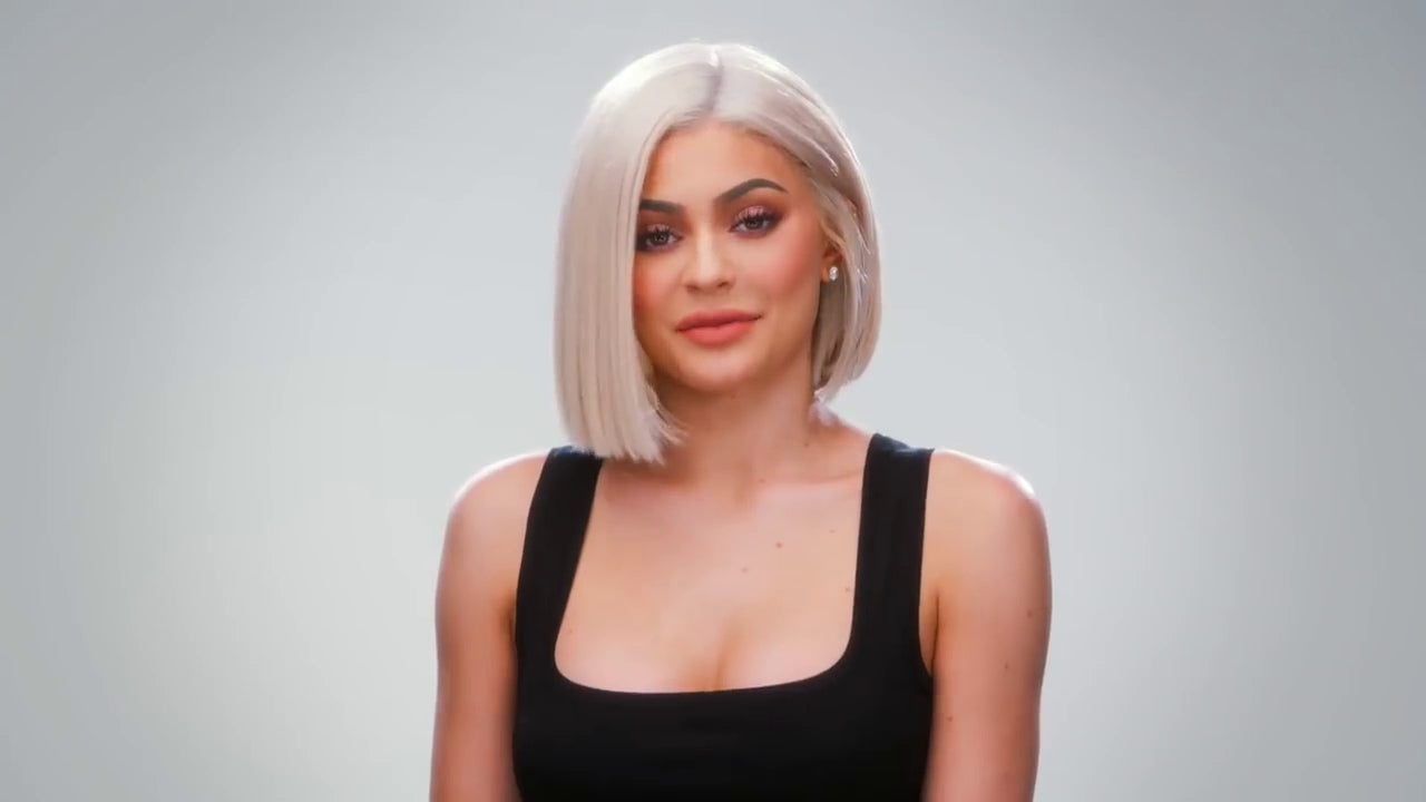 Kylie Jenner wearing a black tank top with a grey bob haircut, posing in front of a light grey background