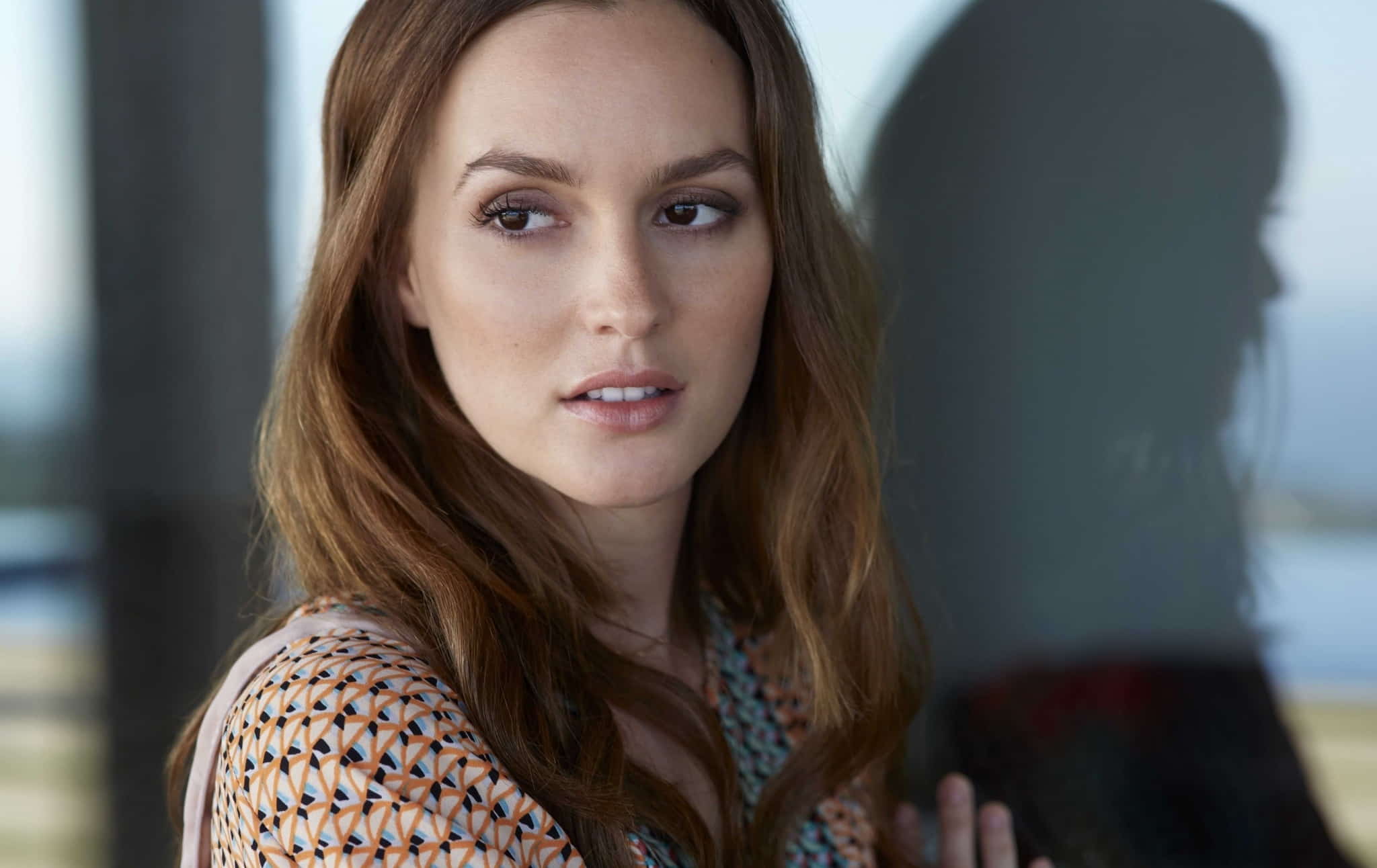 Leighton Meester with wavy brown hair looking to the side, with her reflection in the glass.