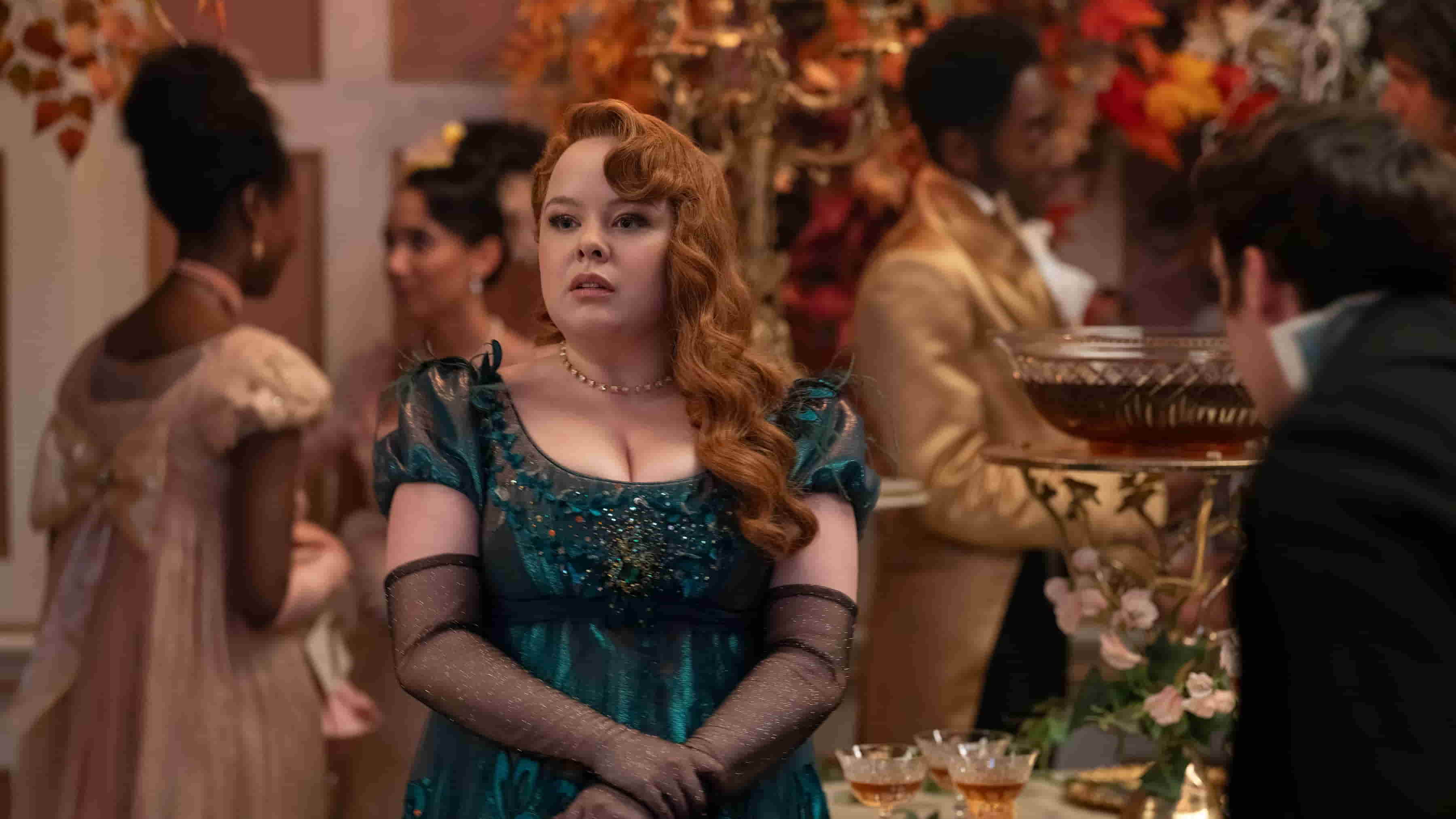 Nicola Coughlan dressed in a regal emerald green gown at a lavish social gathering, with floral decorations, and attendees in period attire.
