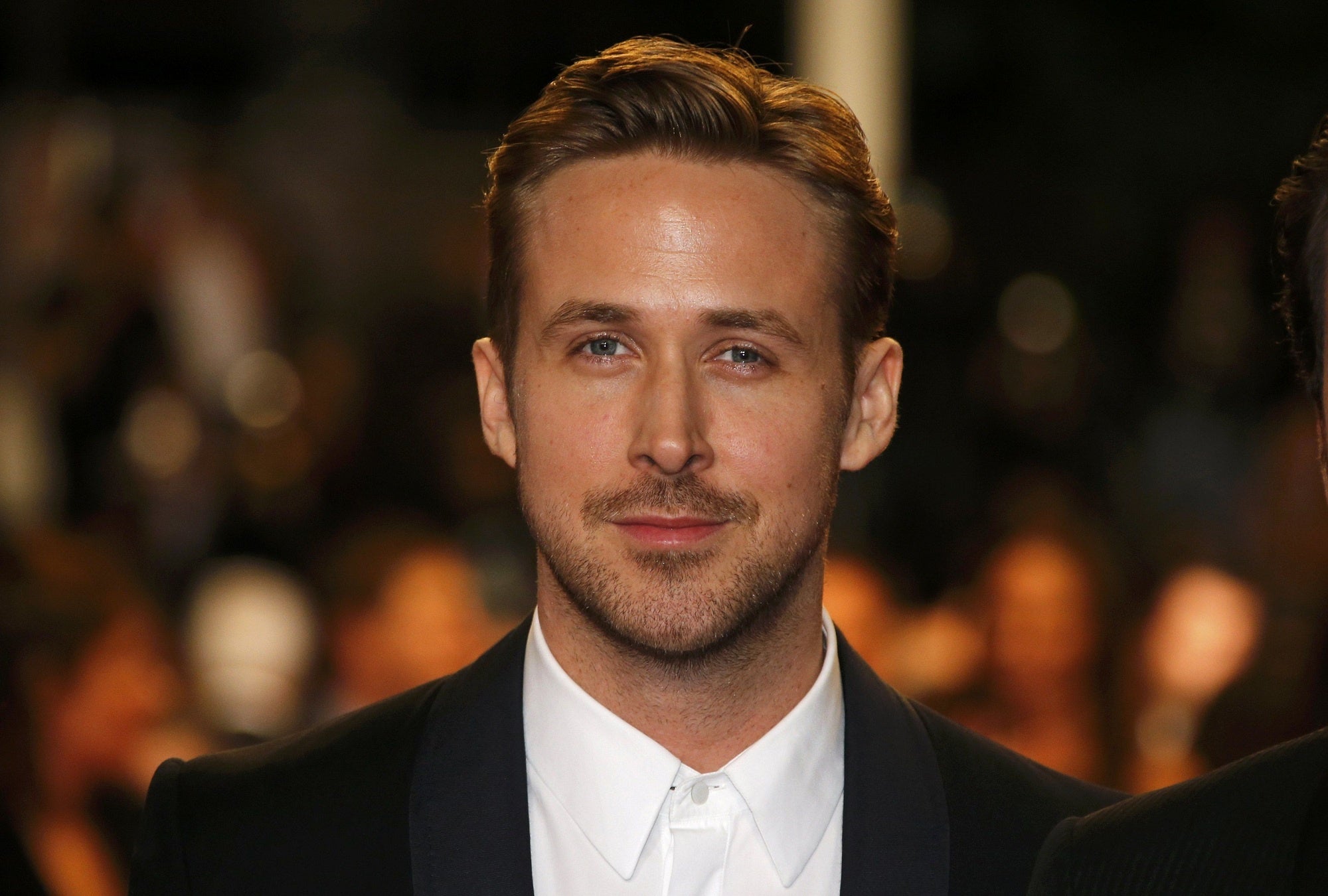 A headshot of actor Ryan Gosling, who is smiling and looking at the camera.