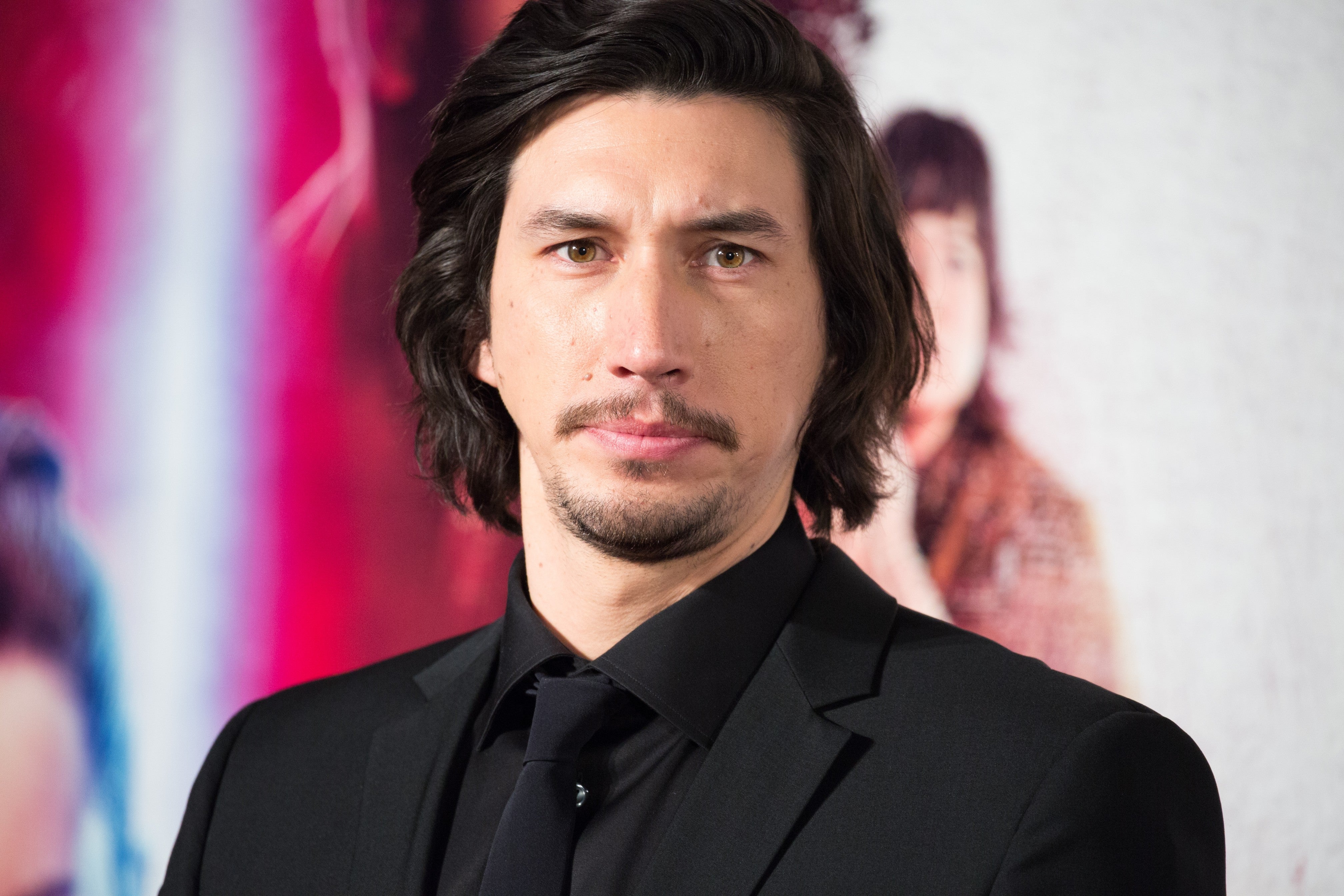 Adam Driver in a black suit looking at the camera