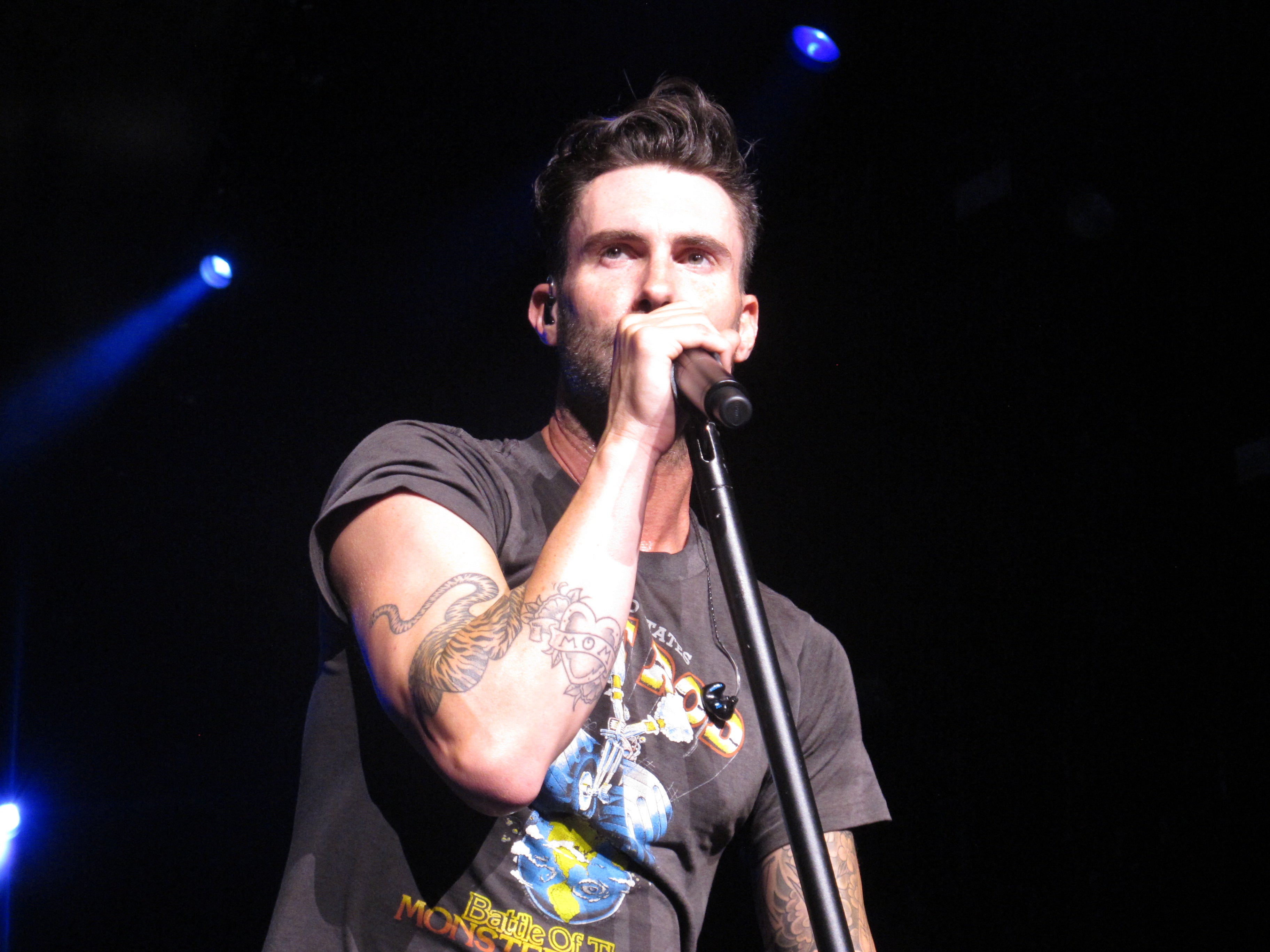 Adam Levine is on stage with a microphone in his hand, singing for the crowd.