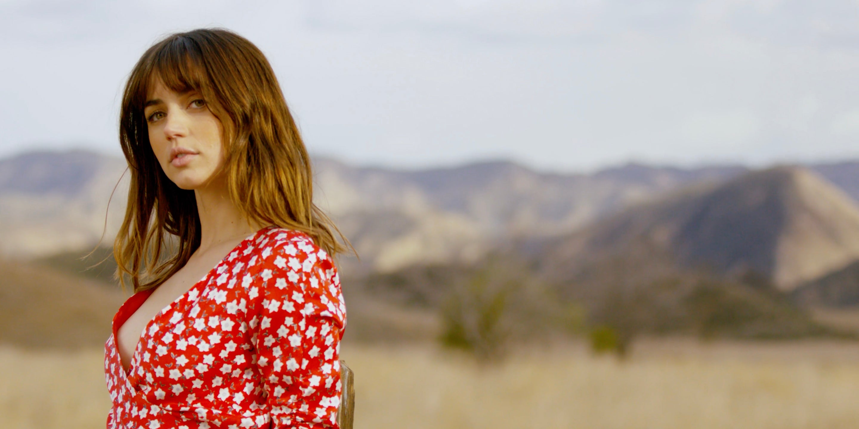 Ana de Armas wearing a red dress and posing for a picture in a natural outdoorsy background