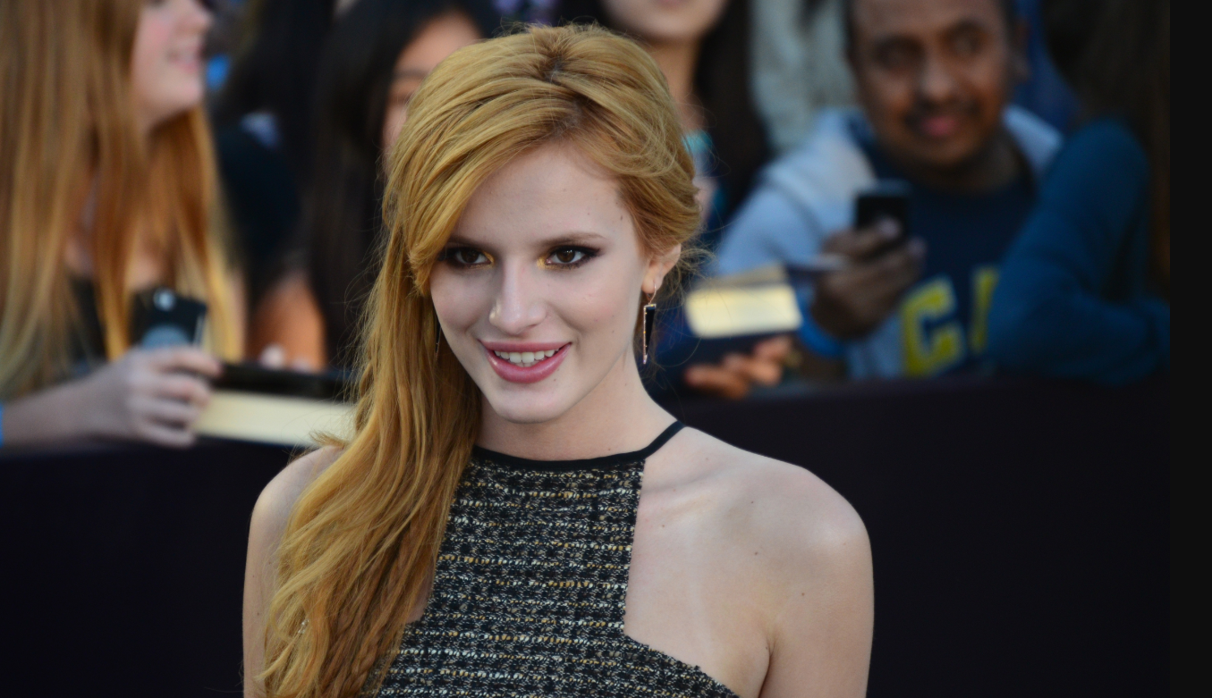 Bella Thorne in a black dress attending an event and smiling for the paparazzi.