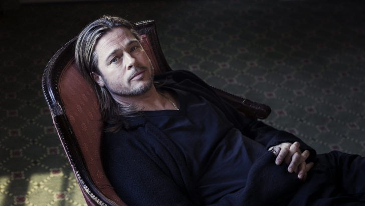 Brad Pitt in all black look sitting on a chair looking up straight into the camera