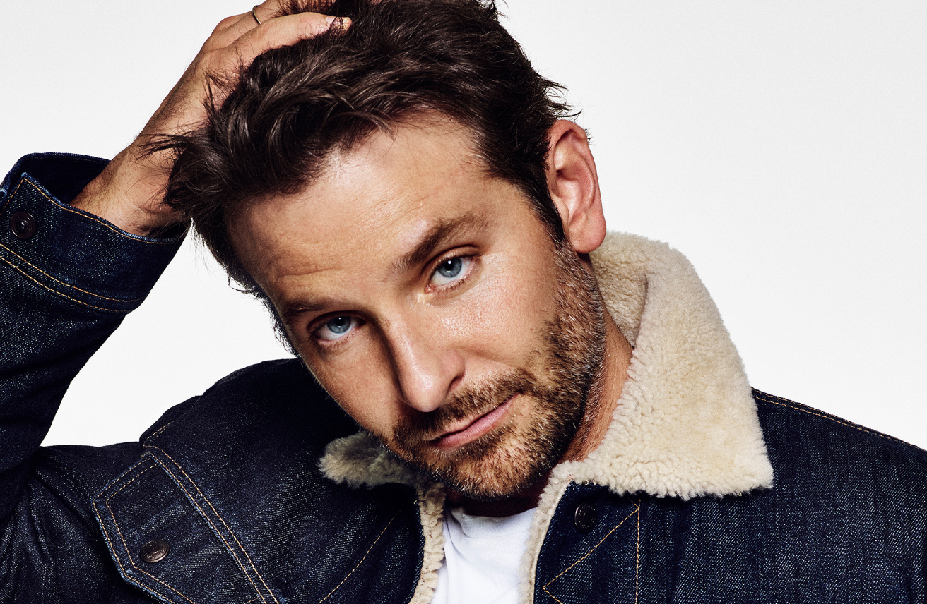 Bradley Cooper wearing a blue denim jacket, posing in front of a white background. 