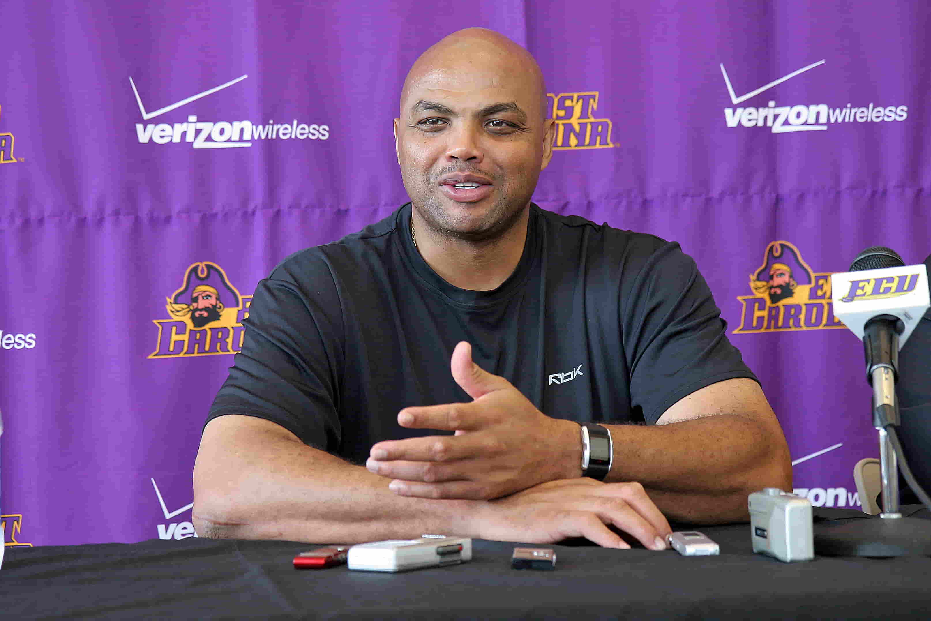 Charles Barkley is sitting at a table with a purple background and a microphone in front of him.