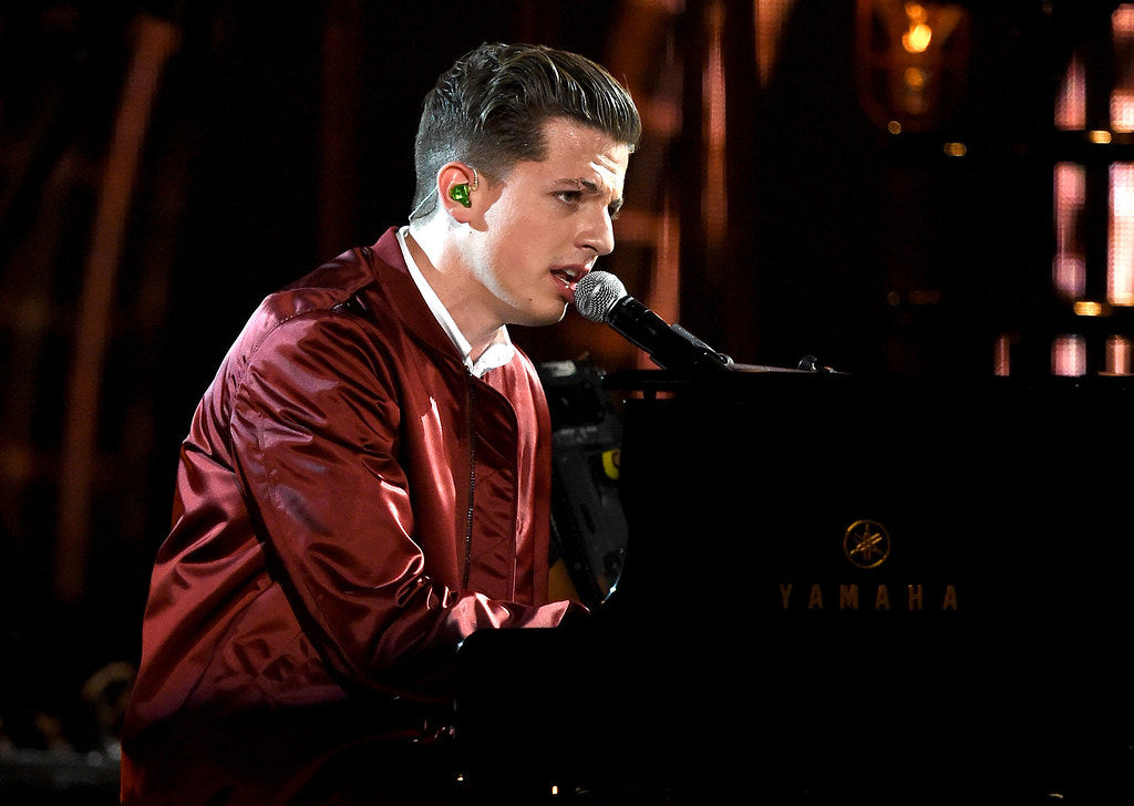 Charlie Puth wearing a maroon jacket on the stage and singing into a microphone 