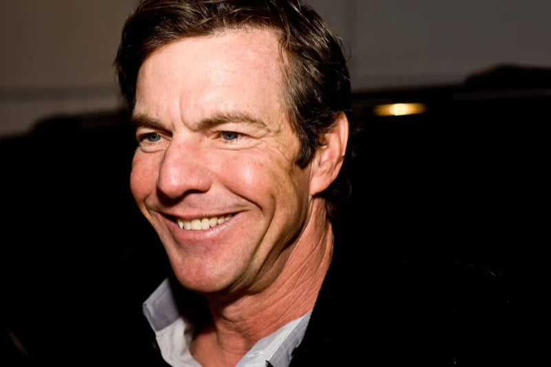 Dennis Quaid is smiling and looking to the left