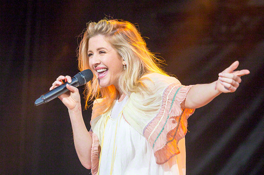 Ellie Goulding in a white flare dress on the stage, holding a microphone in one hand and singing