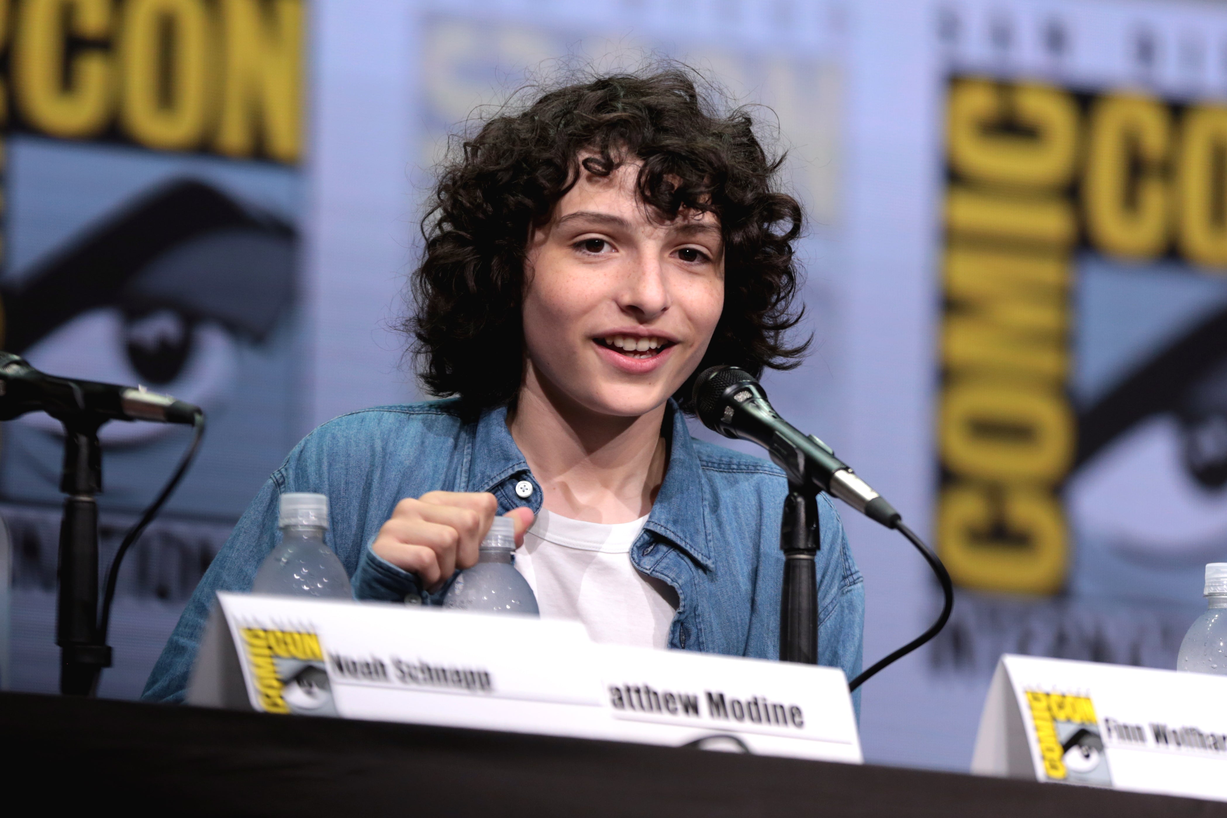 Finn Wolfhard attending a comicon, looking at the camera and smiling.