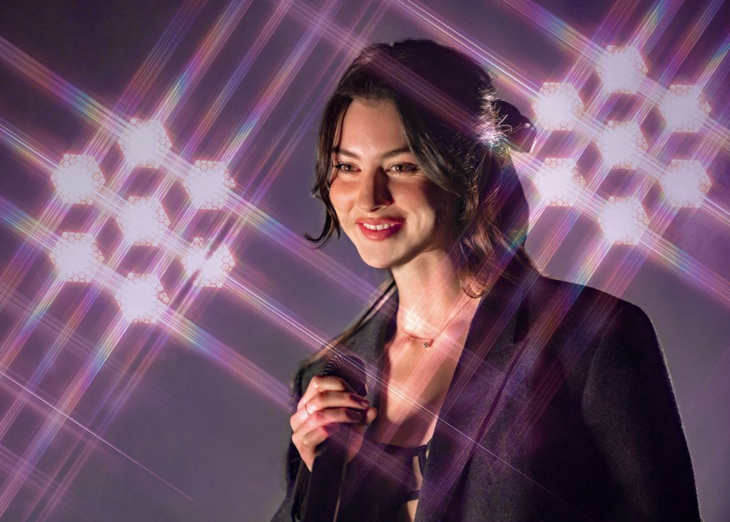 Gracie Abrams on stage, standing against a shiny background, holding a microphone in her hand, and performing for the crowd.