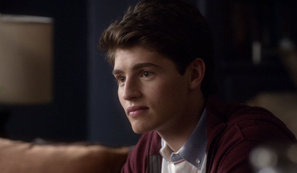 Gregg Sulkin is looking off to the side with a slight smile on his face.