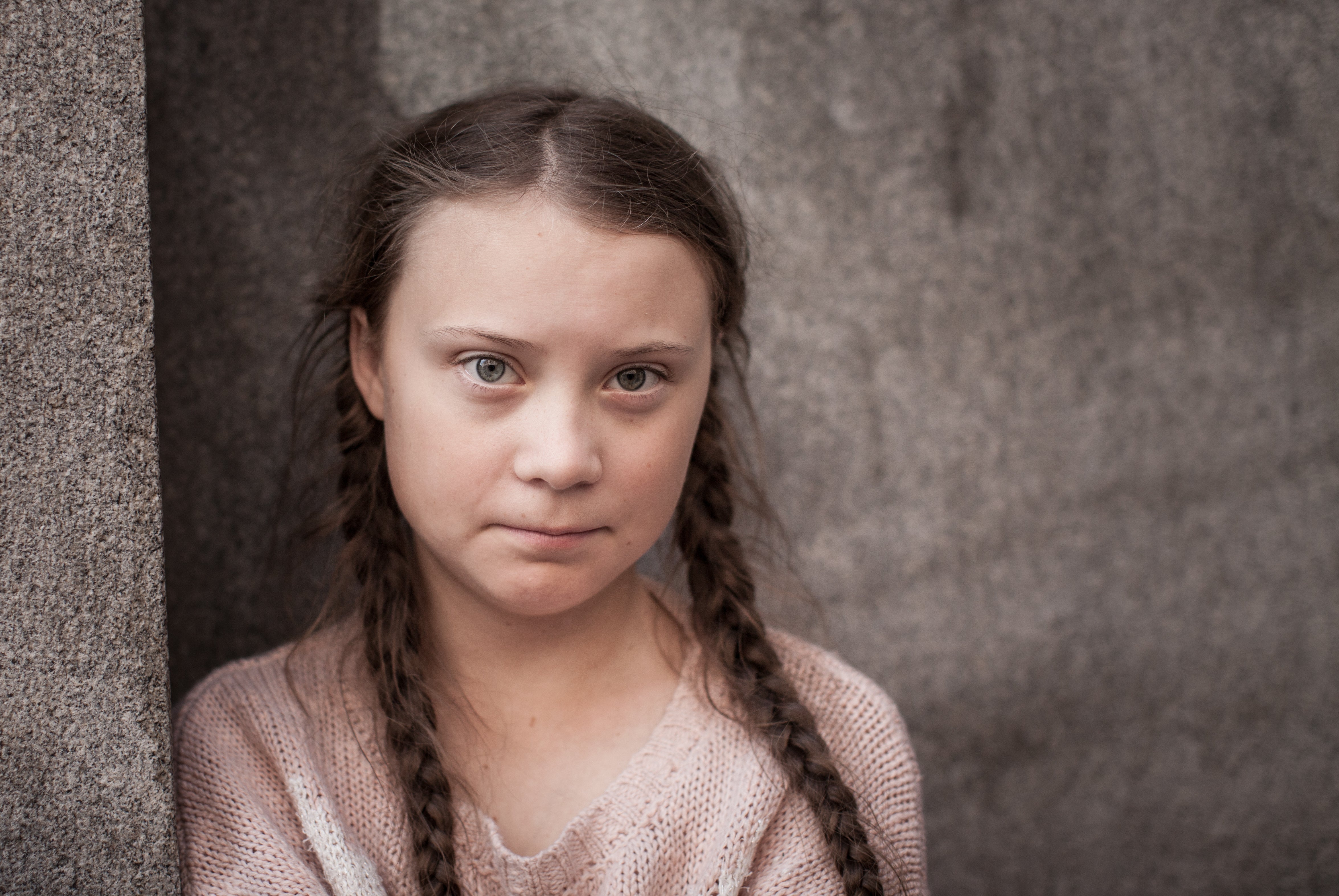 Greta Thunberg in two braids wearing a light pink sweater and looking at the camera