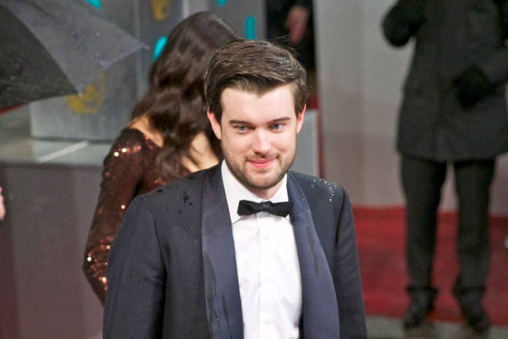 Jack Whitehall in a tuxedo suit, standing at an award function.