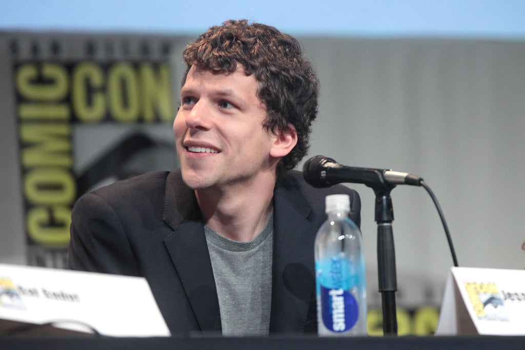 Jesse Eisenberg smiling at a podium during a public speaking event at Comicon.