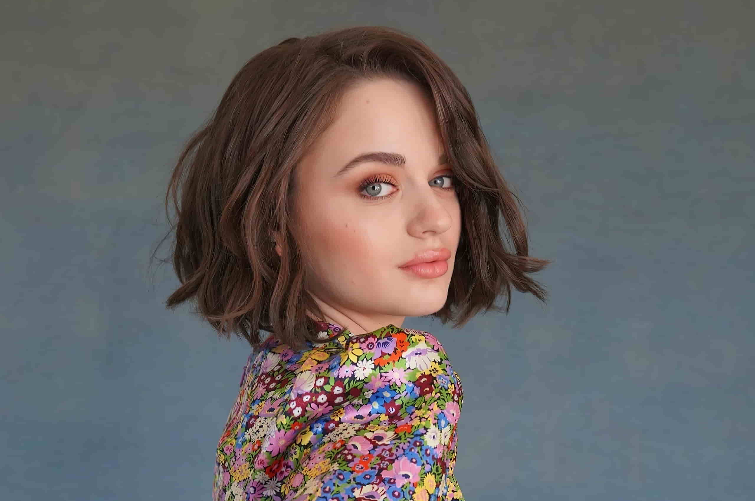 Joey in a floral dress posing in front of a blue background.