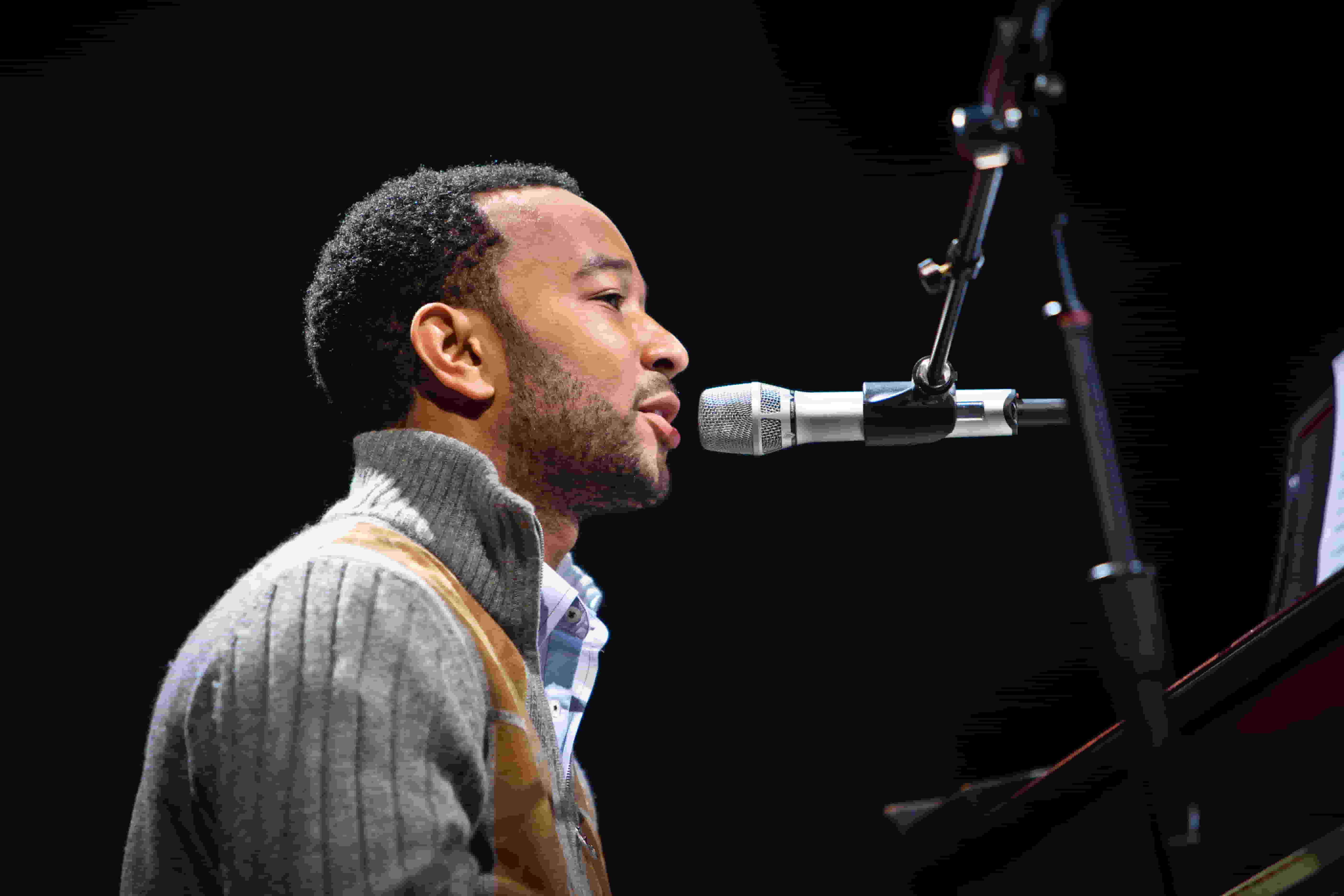 John Legend, dressed in a stylish grey and brown sweater, performing live at his concert.