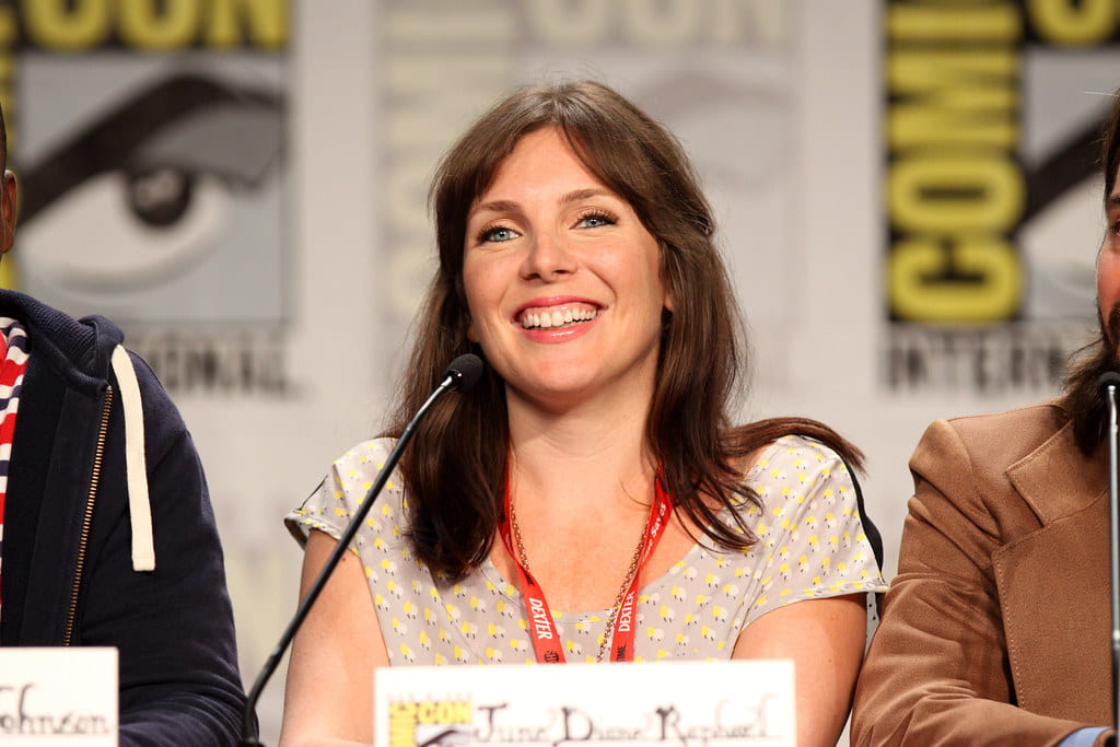 June Diane Raphael wearing a printed top, smiling while addressing the audience at the Comicon event.