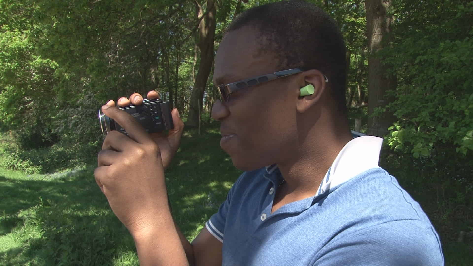 KSI in a light blue t-shirt, holding a video camera and shooting in a jungle 