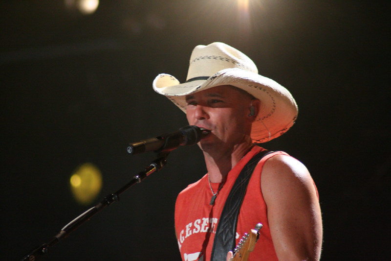 Kenny Chesney on stage singing into a microphone in front of him at a concert