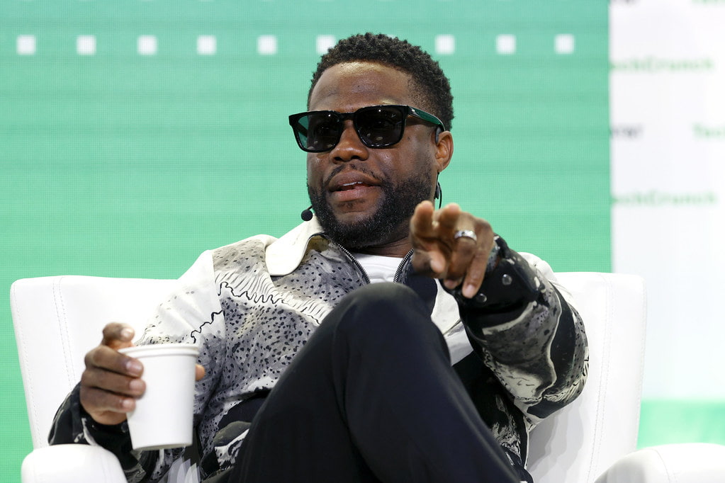 Kevin-Hart at a conference, wearing a black and white printed shirt and black shades