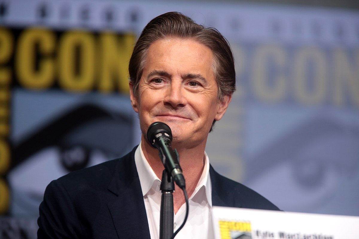 Kyle MacLachlan is  looking at the crowd in front of him at Comic-Con and smiling warmly.