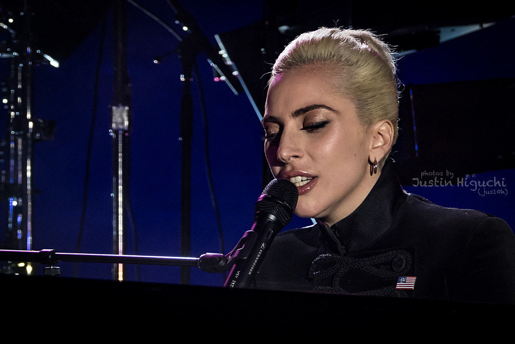 Lady Gaga sitting in front of a piano and singing at a concert 