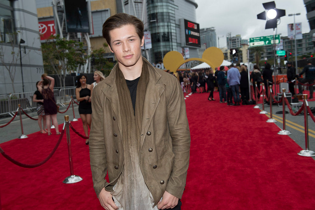 Leo Howard on a red carpet wearing a brown jacket and attending the Disney event 