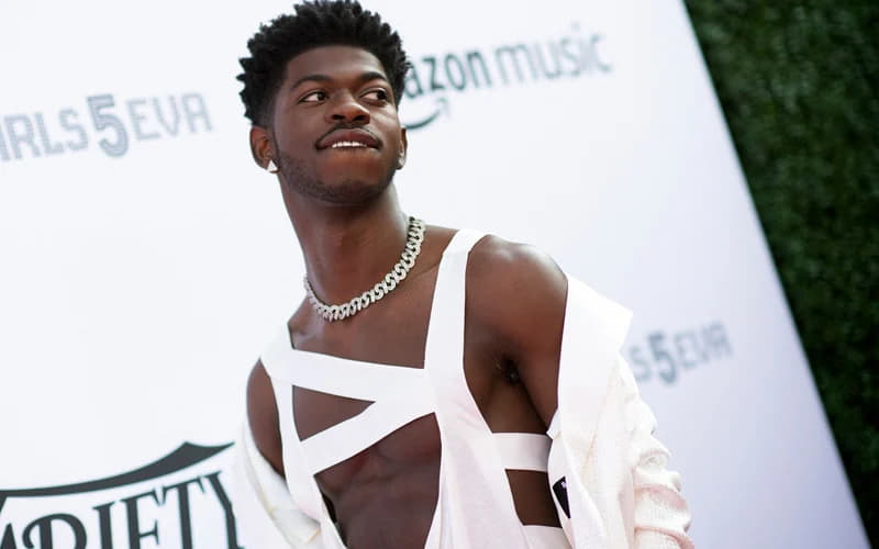 Lil Nas X posing gracefully in a white dress at a music event.