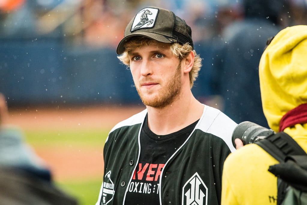 Logan Paul in a black and white jacket and black cap, standing in a play ground