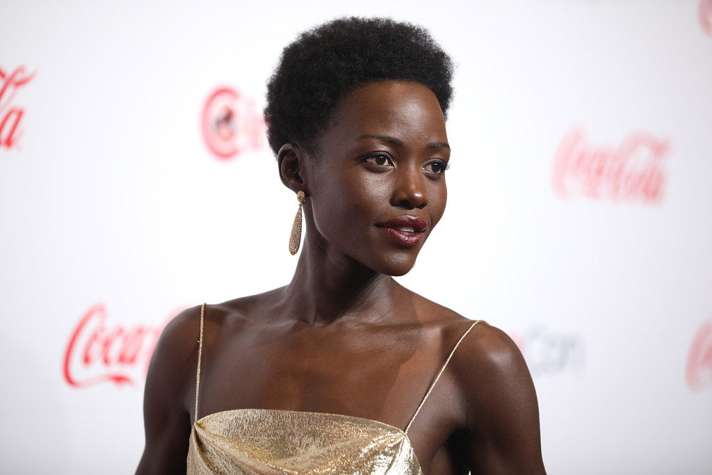 Lupita Nyong in a shimmery dress posing for the camera in front of a white background.