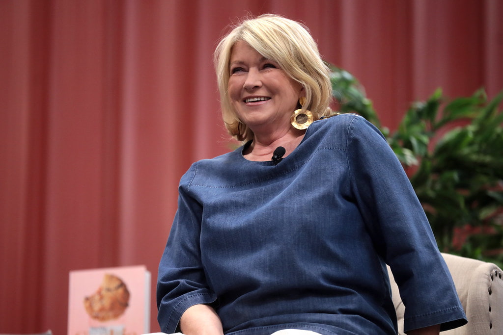 Martha Stewart in a blue dress, smiling while interacting at a conference.