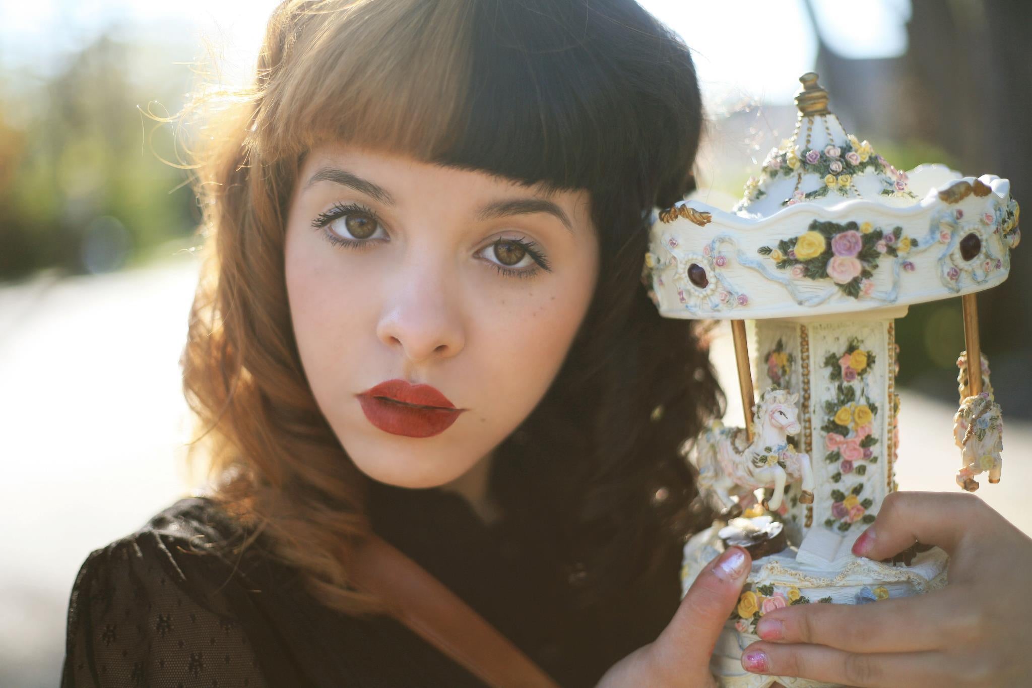 Melanie Martinez holding a carousel music box and looking at the camera with her mouth slightly open.