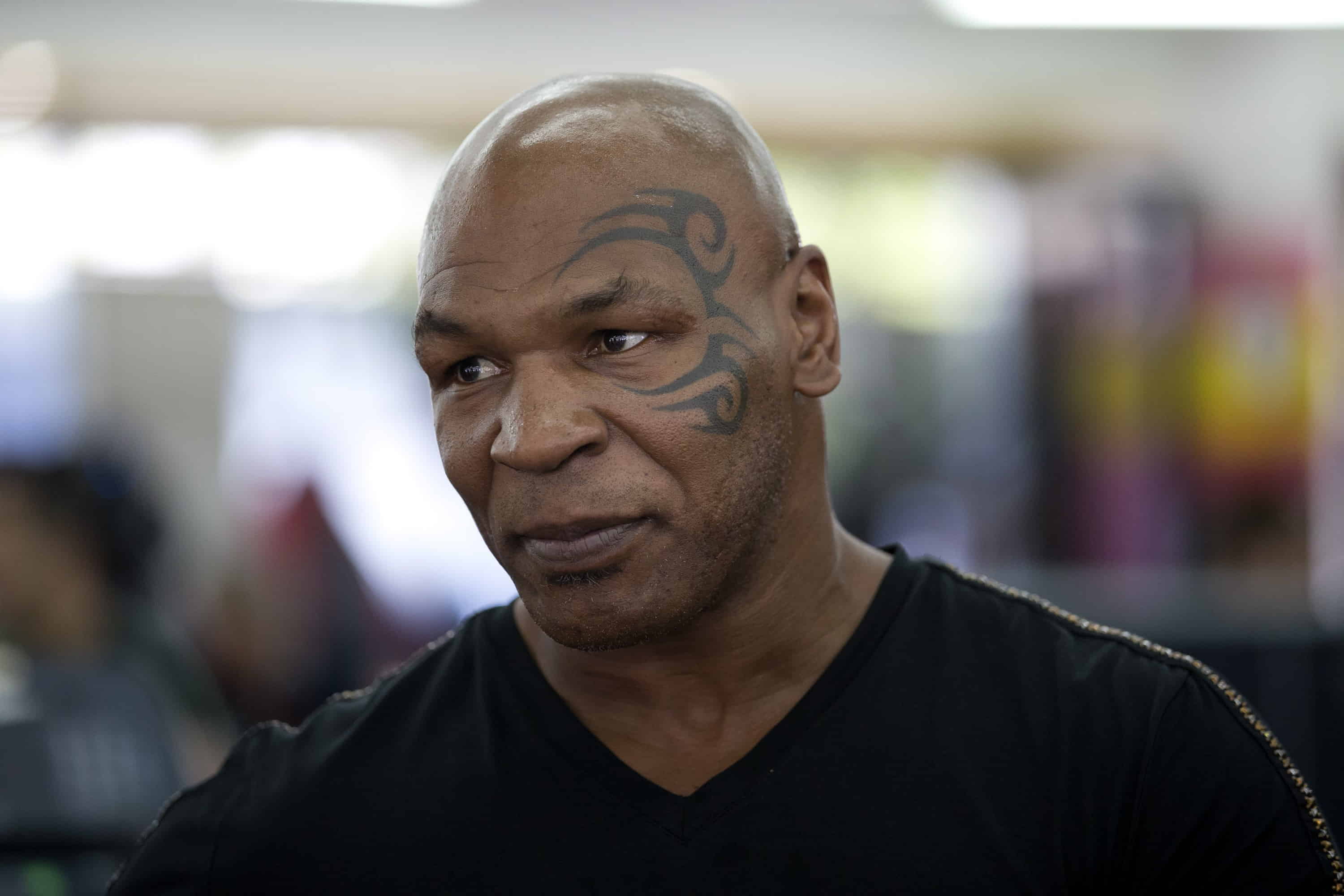 Mike Tyson in a black t-shirt, smiling while looking away from the camera