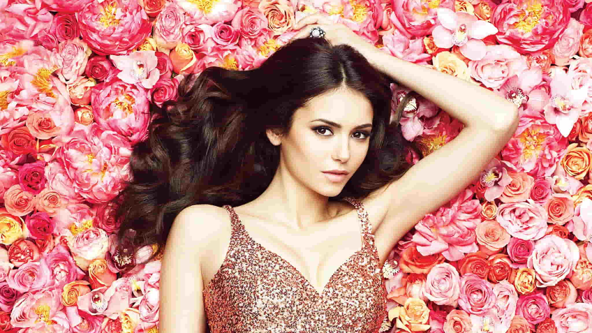 Nina Dobrev in a shimmery dress, laying on pink roses