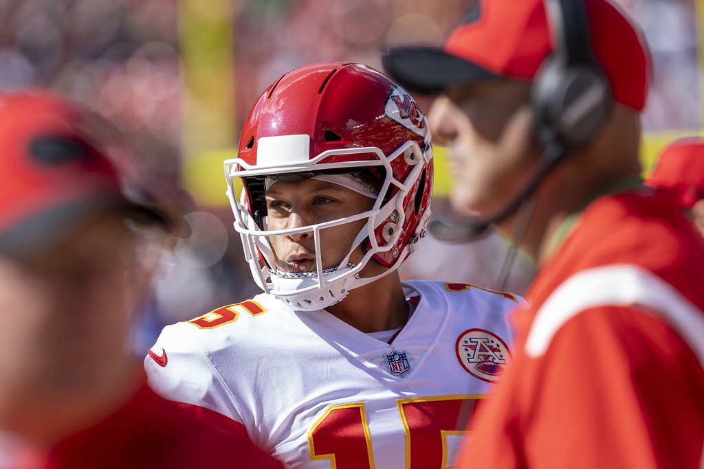 Kansas City Chiefs quarterback Patrick Mahomes is looking to the left while wearing a red helmet and white jersey with red numbers.