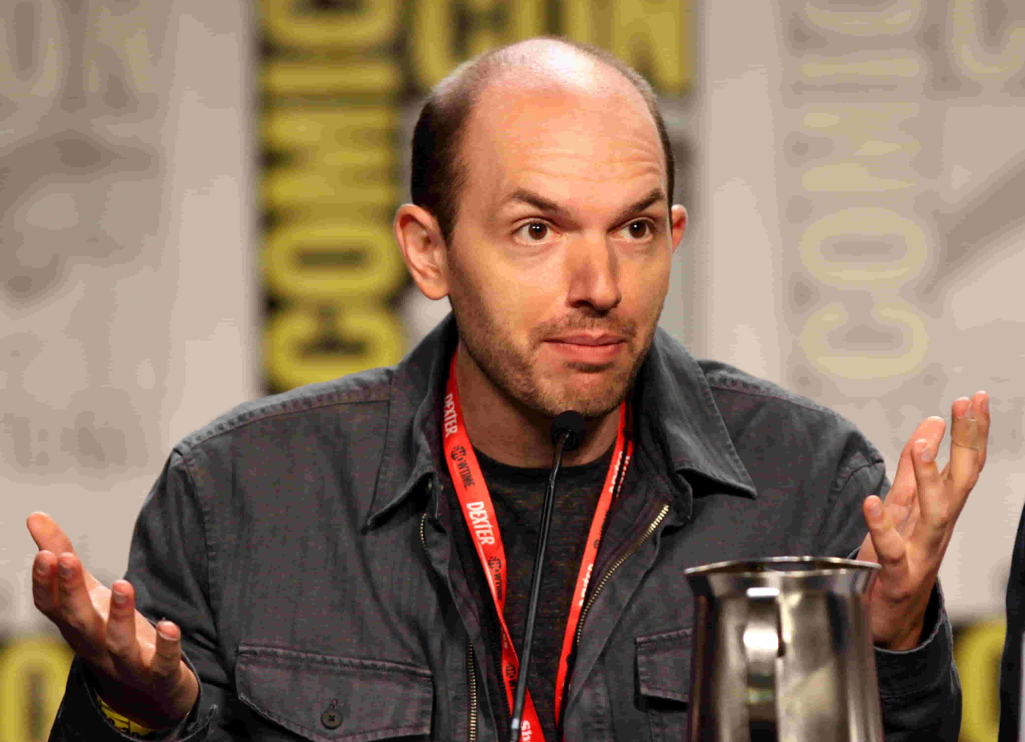 Paul Scheer wearing a denim shirt at the Comicon event, addressing the audience.