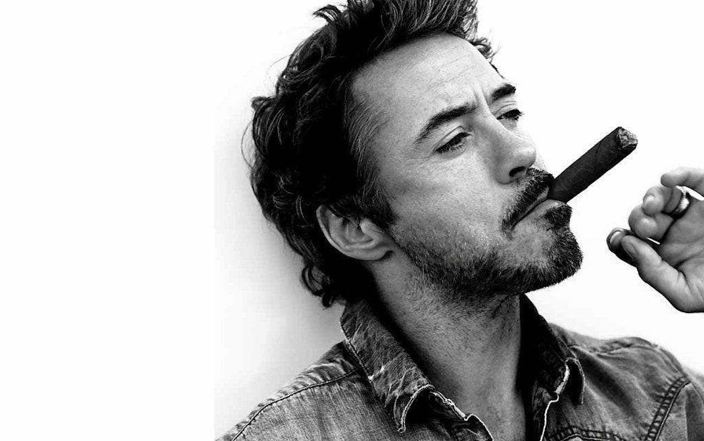 A black and white picture of Robert Downey Jr. where he is smoking a Cuban cigar.