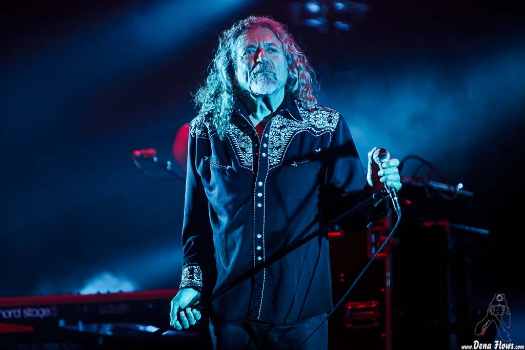 Robert Plant at the music concert with long hair singing into a microphone.