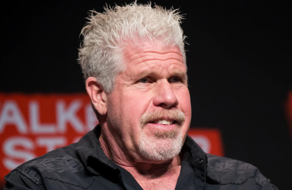 Ron Perlman is wearing a black shirt and looking towards the right side.