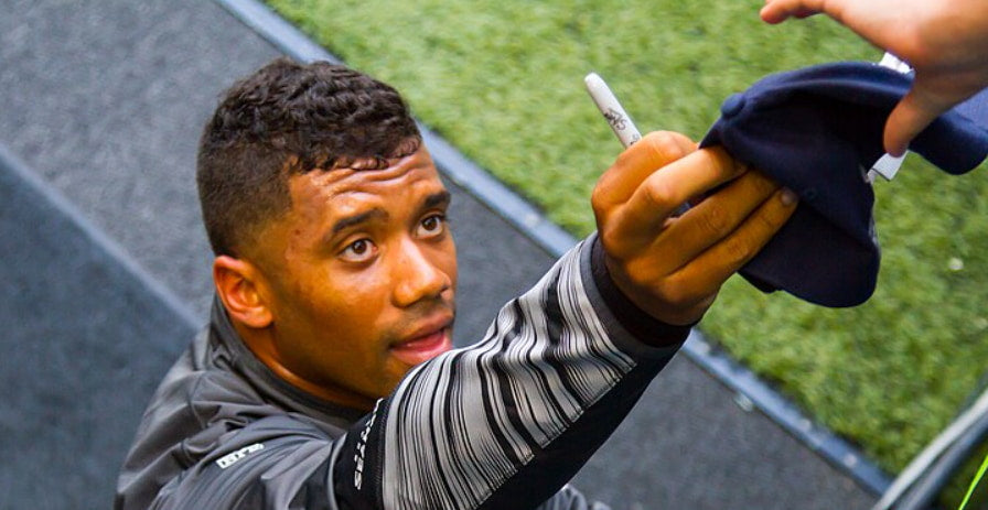 Russell Wilson handing an autographed cap to one of his fans