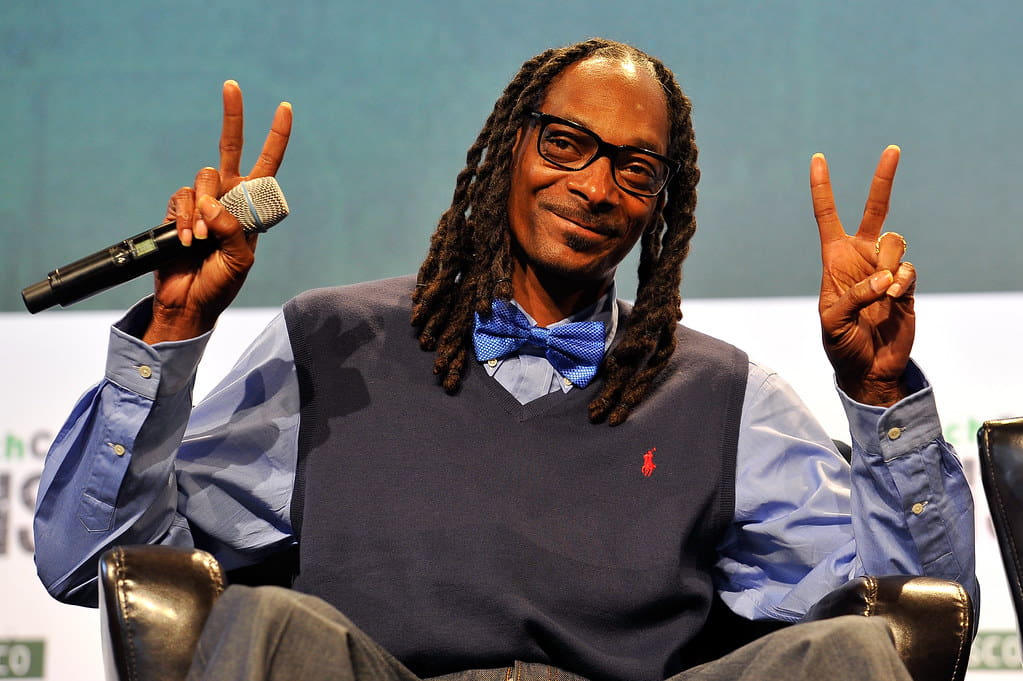 Snoop Dogg holding a microphone and making peace symbol with both his hands